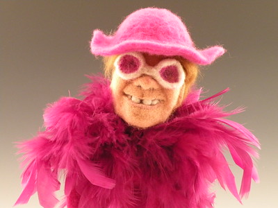 Needle felted Elton John in his needle felted hat and feather boa smiling for the camera the his rose-colored wool glasses.