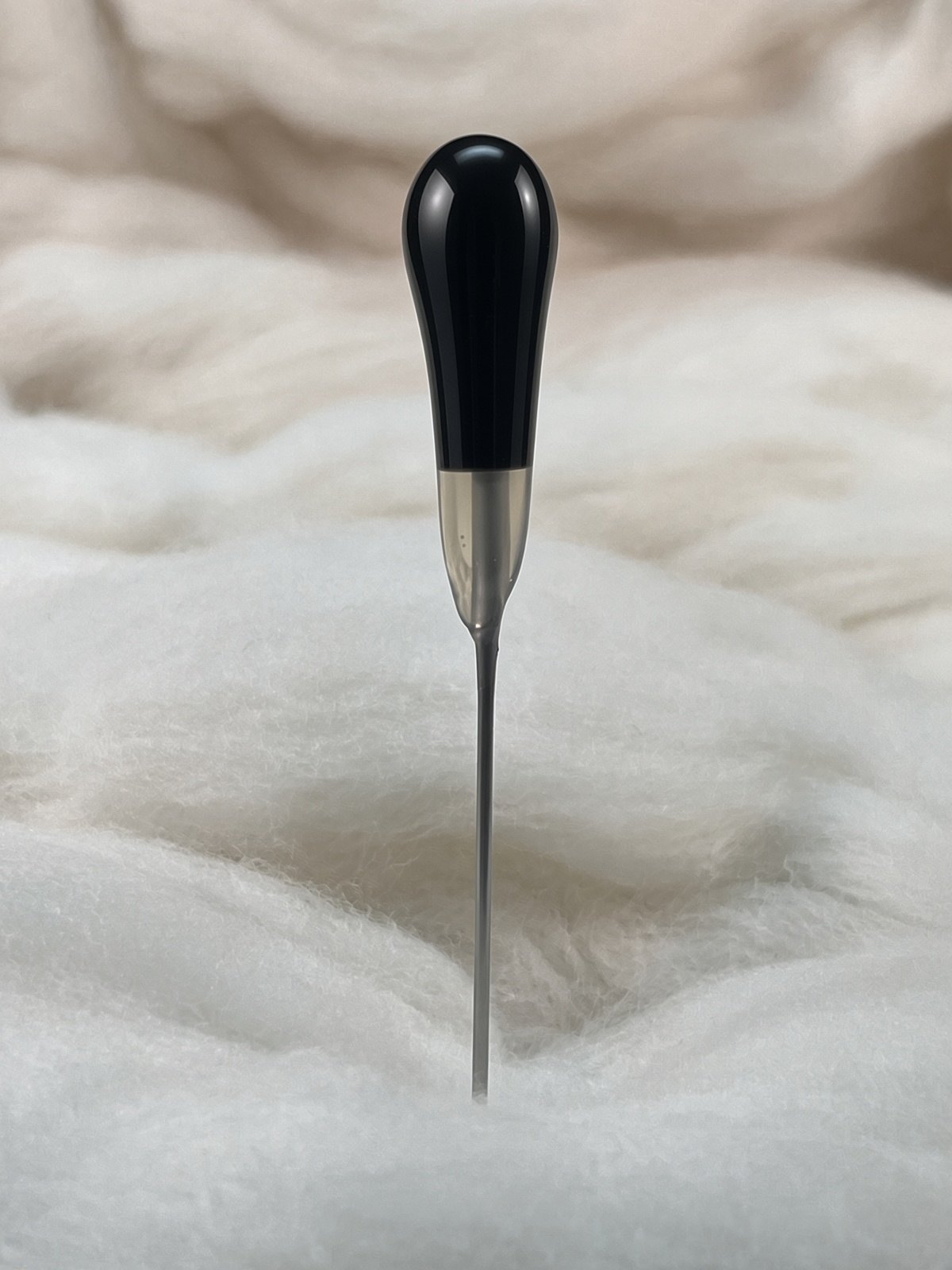 Felt Alive black single felting needle with glossy teardrop handle on natural wool