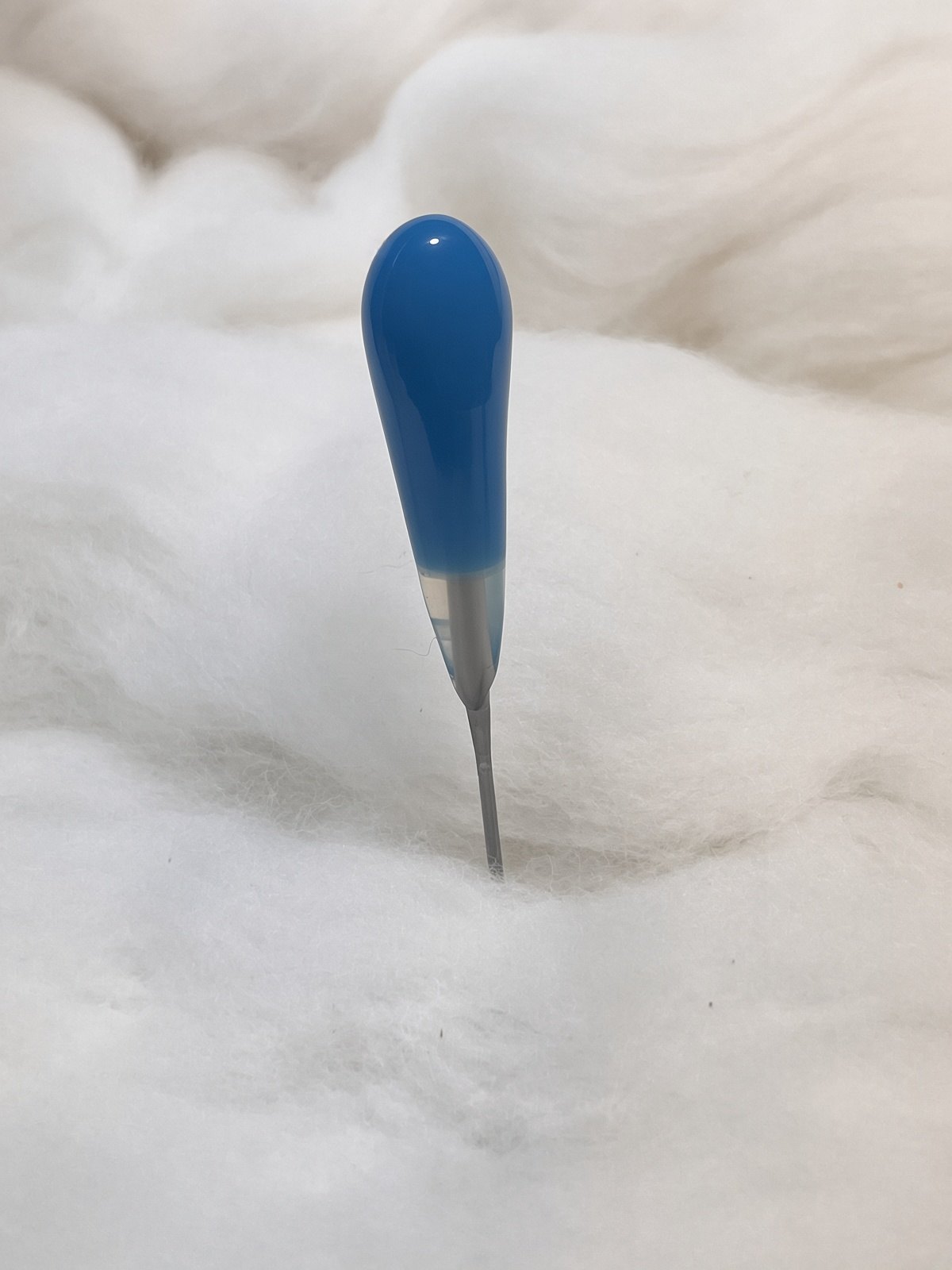 Felt Alive blue single felting needle with glossy teardrop handle on natural wool